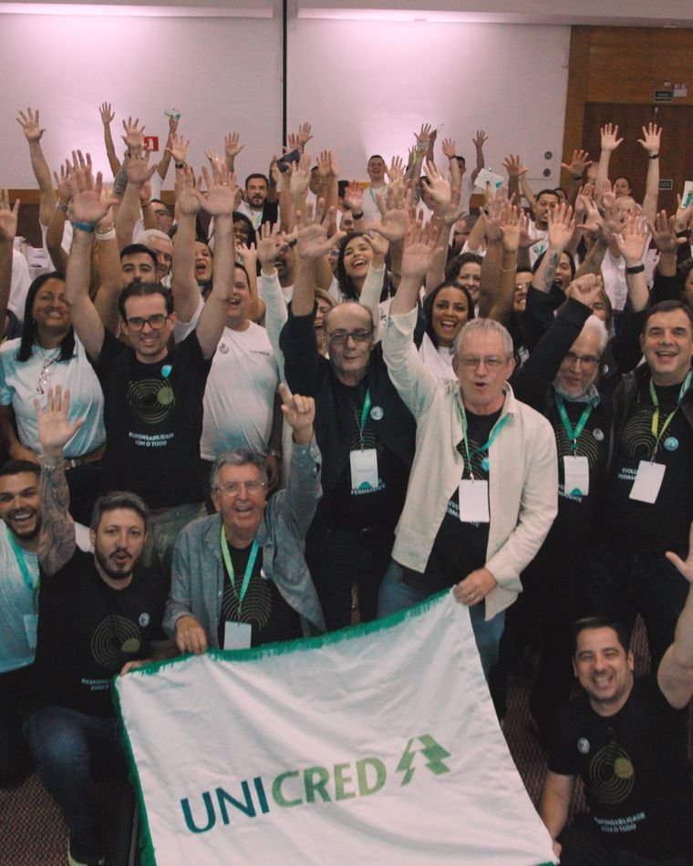 Colaboradores da Unicred Coalizão de braços erguidos, segurando a bandeira da cooperativa no Supera RJ